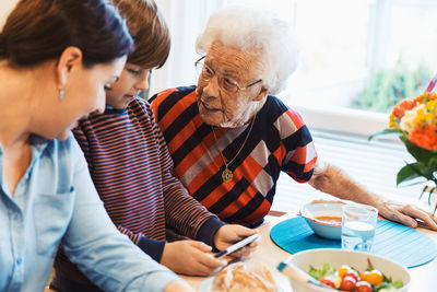 Great grandmother and mother looking at boy using mobile phone in house