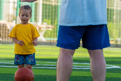 Cute little girl in yellow t-shirt going to kick the ball to father