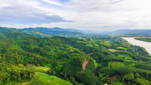 High angle view of green hills by river against cloudy sky