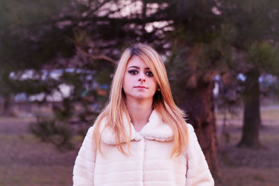 Portrait of beautiful young woman standing against trees