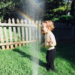 Side view of boy playing by sprinklers in garden