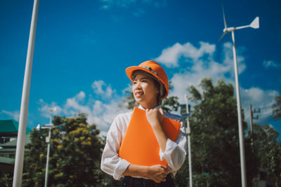 Female engineer in hardhat holding file while standing against windmill