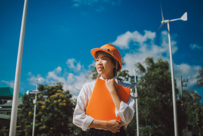 Low angle view of female engineer standing against windmill