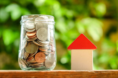 Close-up of coins in glass jar with model house on table at yard