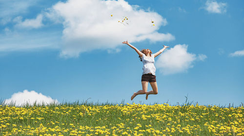 Low angle view of young woman jumping on field against sky