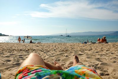 Low section of woman resting on beach against by during sunny day