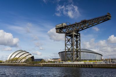 Scottish exhibition and conference centre and finnieston crane by clyde river against blue sky