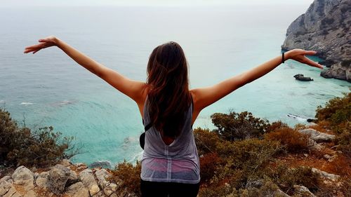 Rear view of young woman standing at beach against sky