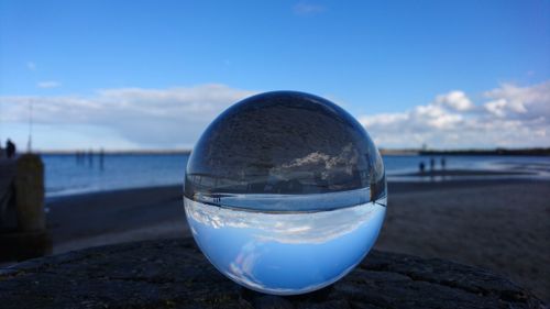 Close-up of crystal ball on beach against blue sky