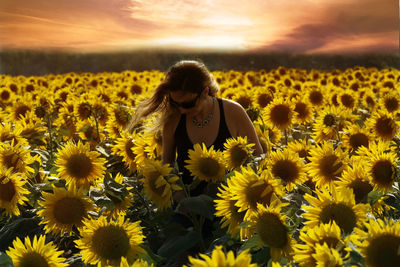 Beautiful woman standing on sunflower field during sunset