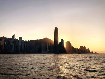 Silhouette buildings by sea against sky during sunset