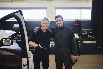 Portrait of happy experts with digital tablet standing at auto repair shop