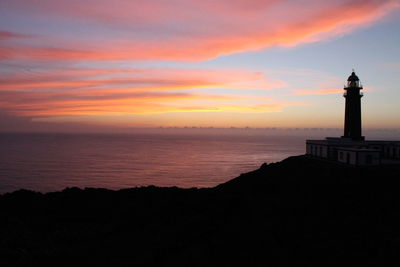 Silhouette lighthouse by sea against sky during sunset