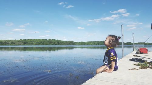 Girl sitting on jetty over lake against sky