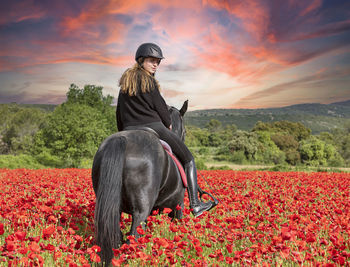 Full length of woman sitting on field against orange sky