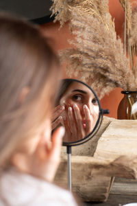 Mirror reflection of woman applying under-eye patch at dressing table closeup