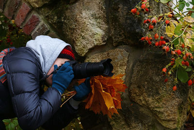 Side view of woman photographing rose hip berries during autumn