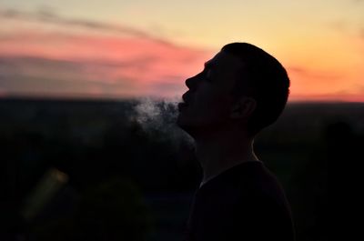 Side view of silhouette man smoking against sky during sunset