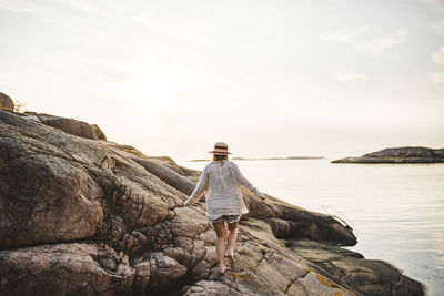 Rear view of man on rock by sea against sky