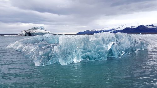 Ice formation floating on sea against cloudy sky