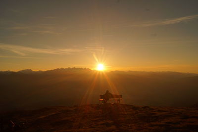 Silhouette of person sitting on bench at sunset