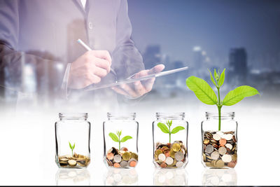 Double exposure image of businessman and coin in jars with seedling on table against city at night