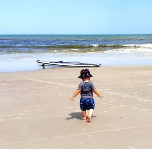 Rear view of boy on beach against sky