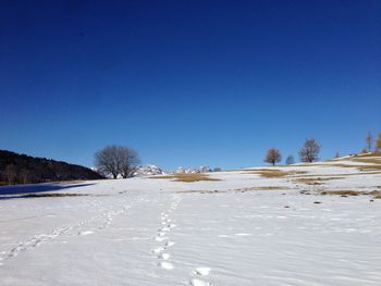 Snow covered field against clear blue sky