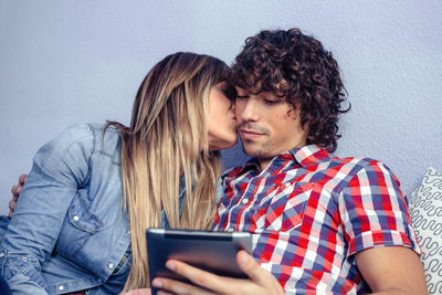 Close-up of woman kissing boyfriend while using digital tablet at home