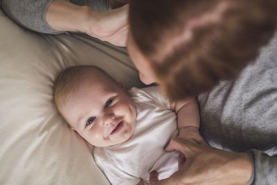 High angle view of mother tickling cute smiling son relaxing on bed at home