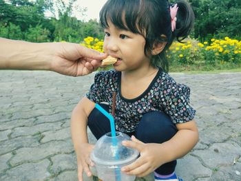 Cropped hand of man feeding daughter on footpath