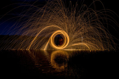 Light trails in lake against sky at night