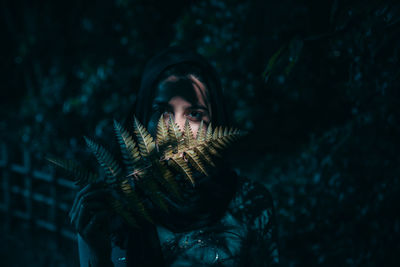 Portrait of young woman holding leaf while standing in park at night