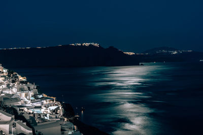 Illuminated city by sea against sky at night