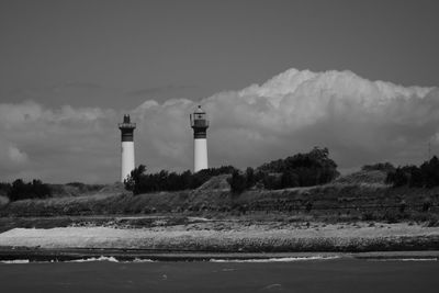 Lighthouse by factory against sky