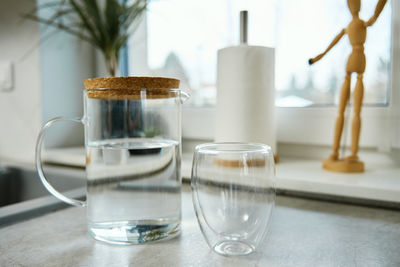 Jug with fresh water and glass on table in kitchen