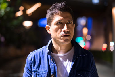 Portrait of young man standing against illuminated city at night