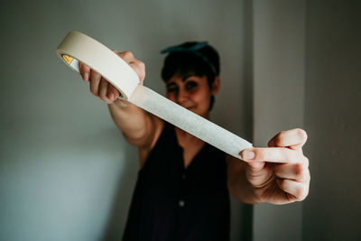 Portrait of woman holding adhesive tape while standing against wall