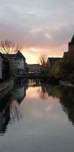 Buildings by lake against sky during sunset