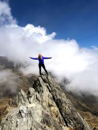 Woman standing on rocky mountain peak against sky