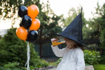 Side view of girl wearing witch hat drinking juice