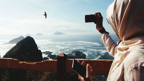 Midsection of woman photographing sea against sky