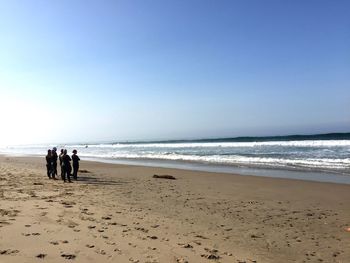 People wearing wetsuit while standing on shore at beach against clear sky