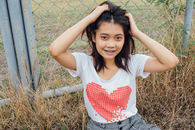 Portrait of young woman standing against fence