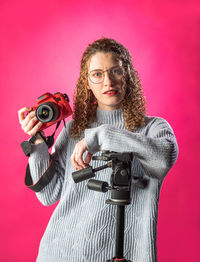 Portrait of young woman with camera against yellow background