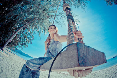 Low angle view of woman sitting on swing at beach