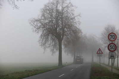 Road by trees on field against sky