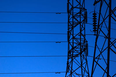 Low angle view of electricity pylon against blue sky