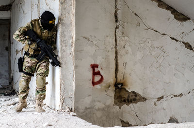 Man holding rifle while standing against wall