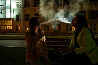 Rear view of woman smoking cigarette on street at night